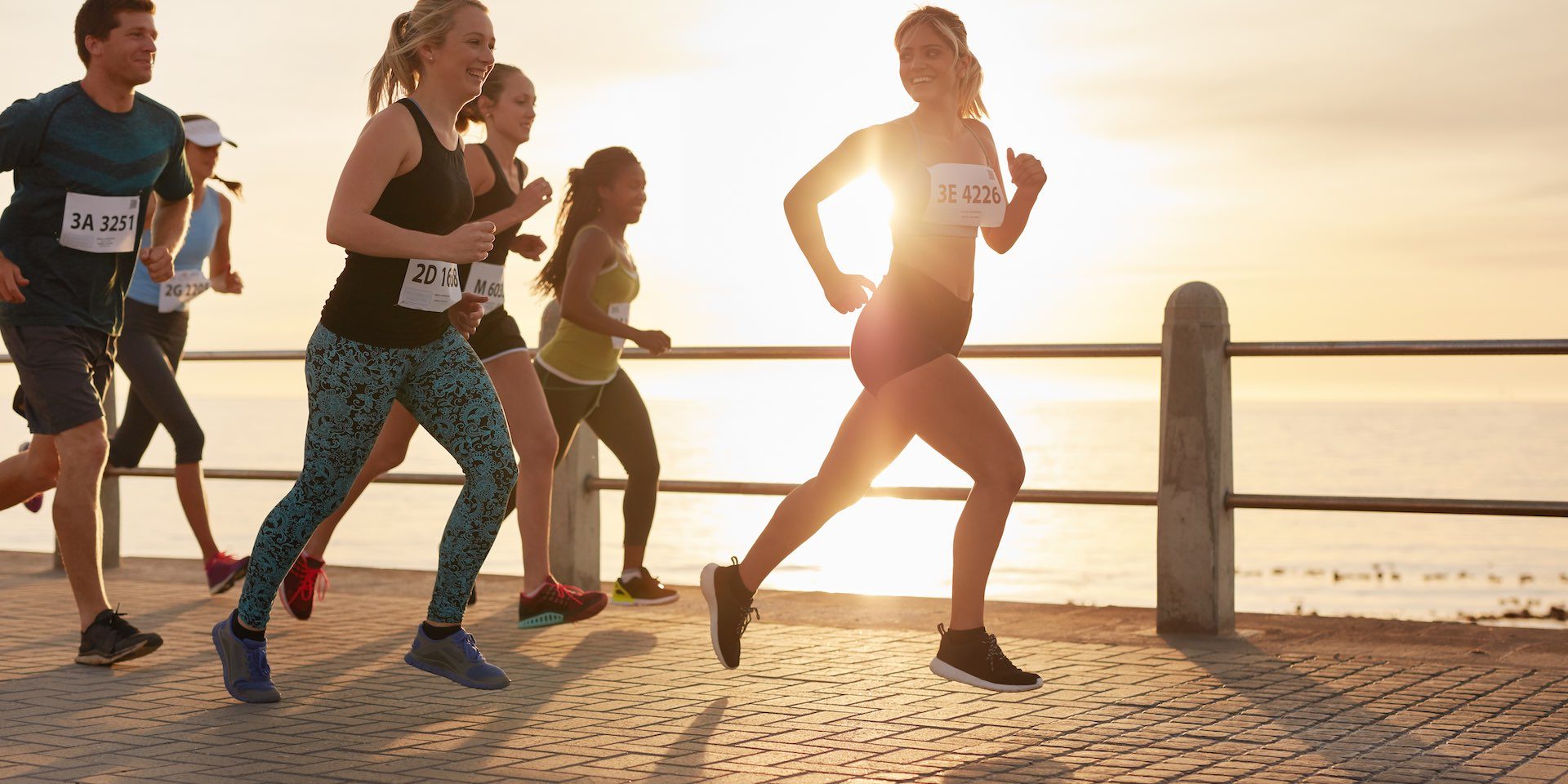 Fit young people running on street by the sea. Runners competing in a marathon race in evening.